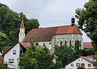 Die Franziskanerkirche in hellgrün ist umgeben von grünen Bäumen und Häusern.