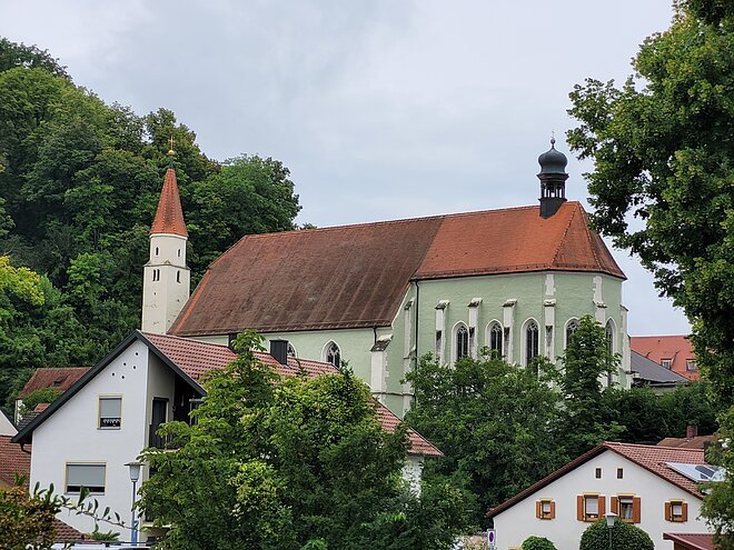 Die Franziskanerkirche in hellgrün ist umgeben von grünen Bäumen und Häusern.